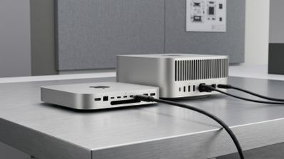 Vista trasera del Mac mini M6 y el Mac Studio M5 Ultra sobre una mesa metálica mostrando sus puertos de conexión y cables conectados.