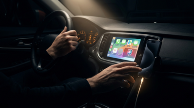 Persona interactuando con la interfaz de CarPlay en la pantalla central de un coche mientras conduce.