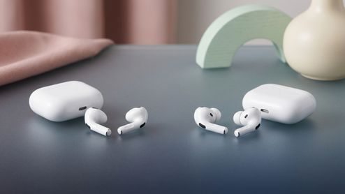 Dos pares de auriculares inalámbricos blancos con sus respectivos estuches de carga sobre una superficie gris.