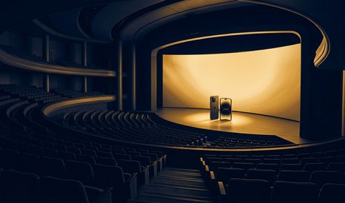 Vista panorámica de un teatro oscuro con una gran pantalla iluminada en el escenario que muestra dos smartphones, uno de ellos plegable.