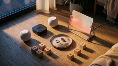 Conjunto de dispositivos Apple en el suelo, incluyendo HomePod mini, Apple TV y una pantalla inteligente experimental, rodeados de iconos de domótica grabados en madera.