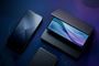 Composición de varios dispositivos electrónicos oscuros incluyendo un teléfono móvil y un ordenador portátil sobre un fondo azul y morado con líneas de circuitos.