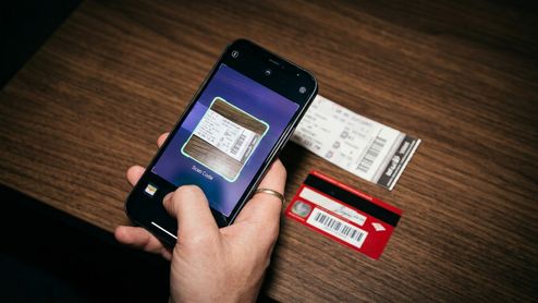 Un iPhone enfoca con su cámara un billete de papel sobre una mesa de madera para escanear su código de barras en Apple Wallet.