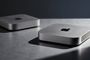 Dos ordenadores Mac mini de color plata situados sobre una superficie metálica bajo una iluminación lateral.