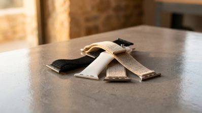 Varias correas para Apple Watch de diferentes materiales y colores apiladas sobre una mesa gris.