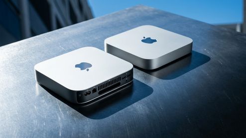 Dos ordenadores Mac mini colocados sobre una superficie metálica, uno mostrando su panel frontal y el otro su parte trasera con puertos de conexión.