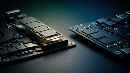 Comparación en primer plano entre una placa base con un módulo SSD M.2 intercambiable elevado y otra placa con chips de almacenamiento NAND soldados directamente en el circuito.