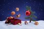 Ilustración en 3D de elementos de los especiales de Peanuts: una calabaza, una cornucopia y un regalo saliendo de una caja roja junto al árbol de Navidad de Charlie Brown en la nieve.