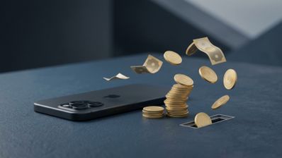 Monedas y billetes volando desde una ranura en una superficie hacia un teléfono iPhone de color oscuro.