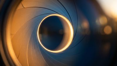 Primer plano de las láminas de un diafragma de cámara fotográfica formando una apertura circular iluminada.