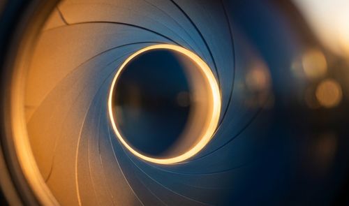 Primer plano de las láminas de un diafragma de cámara fotográfica formando una apertura circular iluminada.