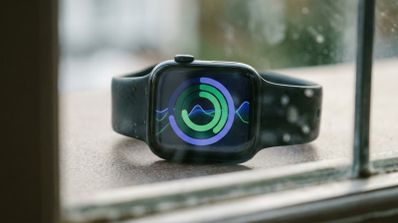 Reloj inteligente Apple Watch con pantalla que muestra gráficos circulares de actividad y ondas de datos sobre un fondo azul.