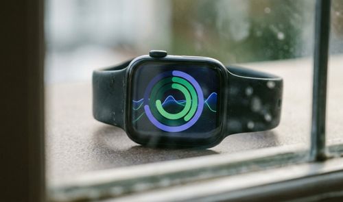 Reloj inteligente Apple Watch con pantalla que muestra gráficos circulares de actividad y ondas de datos sobre un fondo azul.