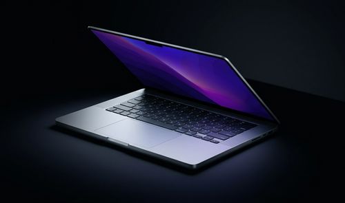 MacBook Pro de 14 pulgadas parcialmente abierto sobre una superficie oscura con fondo negro.