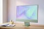 Ordenador todo en uno iMac de color verde sobre una mesa de madera con un cuaderno y un bolígrafo al lado.