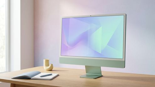 Ordenador todo en uno iMac de color verde sobre una mesa de madera con un cuaderno y un bolígrafo al lado.