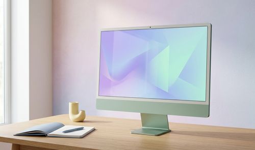 Ordenador todo en uno iMac de color verde sobre una mesa de madera con un cuaderno y un bolígrafo al lado.