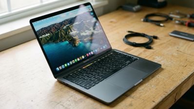 MacBook Pro abierto sobre una mesa de madera con varios cables y accesorios de fondo.