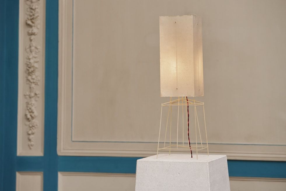 Lámpara de diseño minimalista sobre un pedestal blanco en una sala con molduras clásicas.