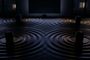 Representación conceptual de cuatro altavoces HomePod situados frente a un televisor, generando ondas de sonido circulares en una superficie oscura.
