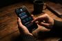 Manos sujetando un iPhone en modo oscuro con la opción de bloquear remitente seleccionada en la aplicación Mensajes.