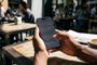 Manos de una persona sosteniendo un iPhone con el menú de ajustes de accesibilidad abierto en la terraza de una cafetería.