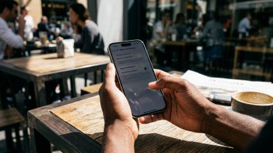 Manos de una persona sosteniendo un iPhone con el menú de ajustes de accesibilidad abierto en la terraza de una cafetería.