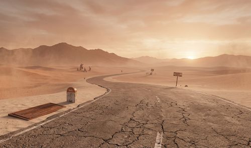 Carretera agrietada y sinuosa que atraviesa un desierto de arena bajo un cielo anaranjado al atardecer.