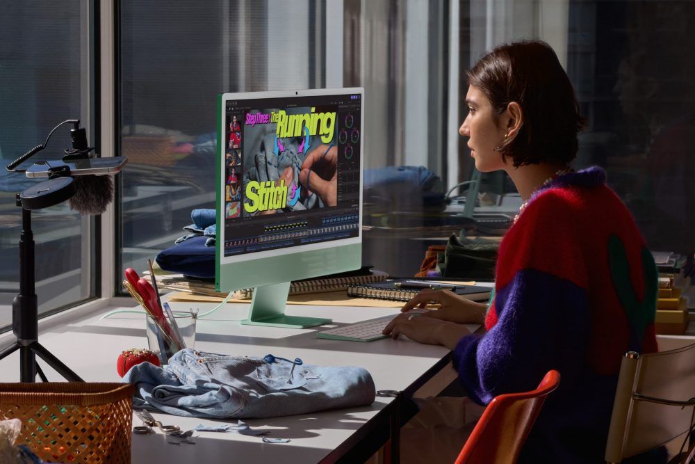 Una mujer utiliza un iMac de color verde para editar un vídeo de costura en un escritorio junto a un ventanal.