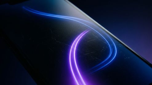 Plano detalle de la pantalla de un smartphone con una estela de luz azul y violeta en forma de onda.