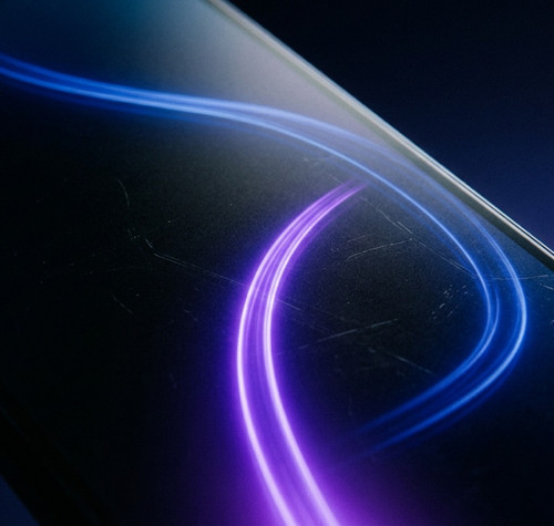 Plano detalle de la pantalla de un smartphone con una estela de luz azul y violeta en forma de onda.