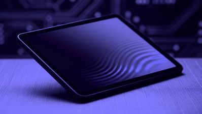 Tableta iPad mini situada en ángulo sobre una superficie con fondo de circuitos, bajo una iluminación de tonos violetas.