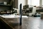 Vista de perfil de un smartphone extremadamente fino de color azul oscuro colocado verticalmente sobre una mesa de trabajo de madera en un taller.