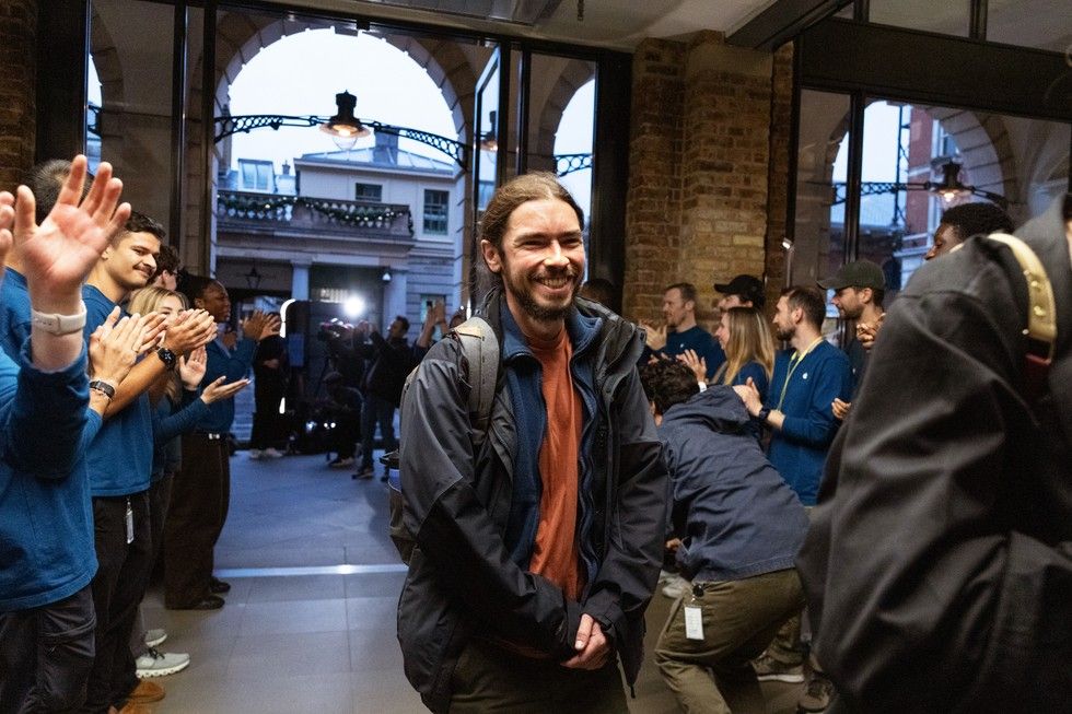 Un cliente sonriente entra en una Apple Store mientras los empleados, situados en dos filas, le reciben con aplausos.