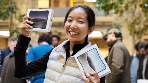 Una mujer sonríe en una Apple Store mientras sostiene dos cajas del iPhone Duo plegable.