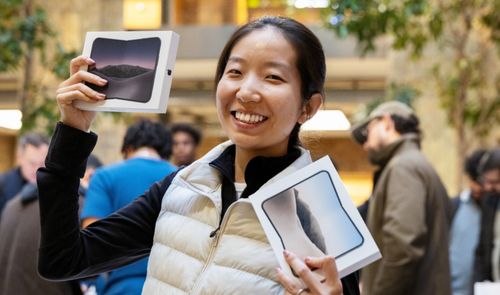 Una mujer sonríe en una Apple Store mientras sostiene dos cajas del iPhone Duo plegable.
