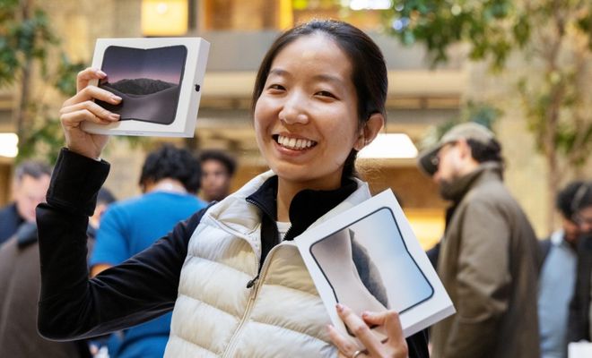 Una mujer sonríe en una Apple Store mientras sostiene dos cajas del iPhone Duo plegable.