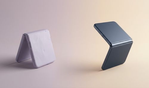 Dos teléfonos plegables tipo concha apoyados sobre sus marcos en una superficie plana con fondo degradado.