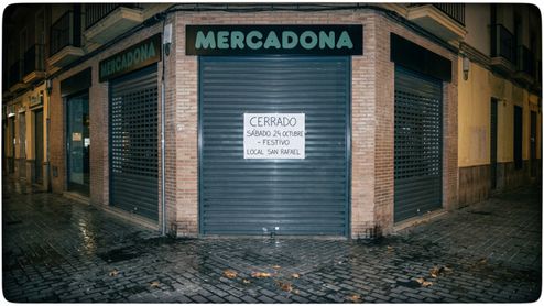 Fachada de un supermercado Mercadona con el cierre metálico bajado y un cartel de aviso por festivo local.
