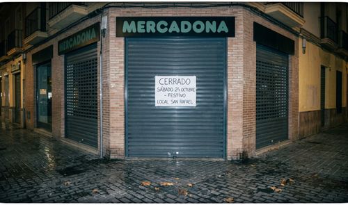 Fachada de un supermercado Mercadona con el cierre metálico bajado y un cartel de aviso por festivo local.