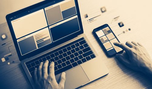 Persona utilizando simultáneamente un ordenador portátil y un teléfono móvil que muestran una interfaz de navegación web organizada por bloques.