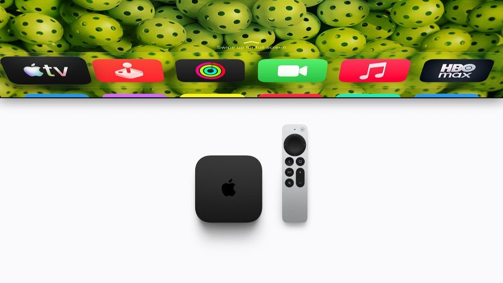 Consola Apple TV 4K de color negro junto al mando Siri Remote sobre un fondo blanco, con una sección de la interfaz de tvOS visible en la parte superior.
