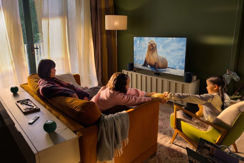 Tres personas en un salón consumiendo contenido en un televisor conectado a un Apple TV 4K y altavoces HomePod.