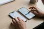 Una persona gestiona simultáneamente los ajustes de transferencia de eSIM en un iPhone y un smartphone Android situados sobre una mesa de madera.