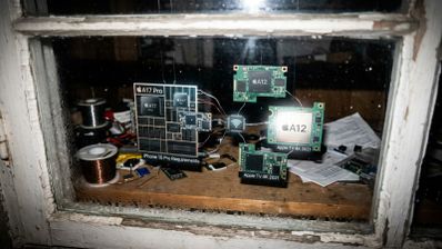 Montaje fotográfico sobre un taller de electrónica que compara los requisitos de hardware entre el chip A17 Pro y el chip A12.