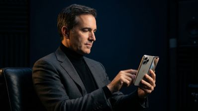 John Ternus sentado de perfil manejando un iPhone Duo con la pantalla abierta.