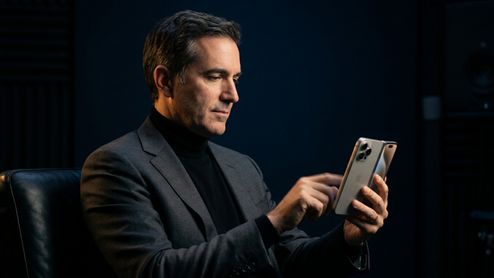 John Ternus sentado de perfil manejando un iPhone Duo con la pantalla abierta.